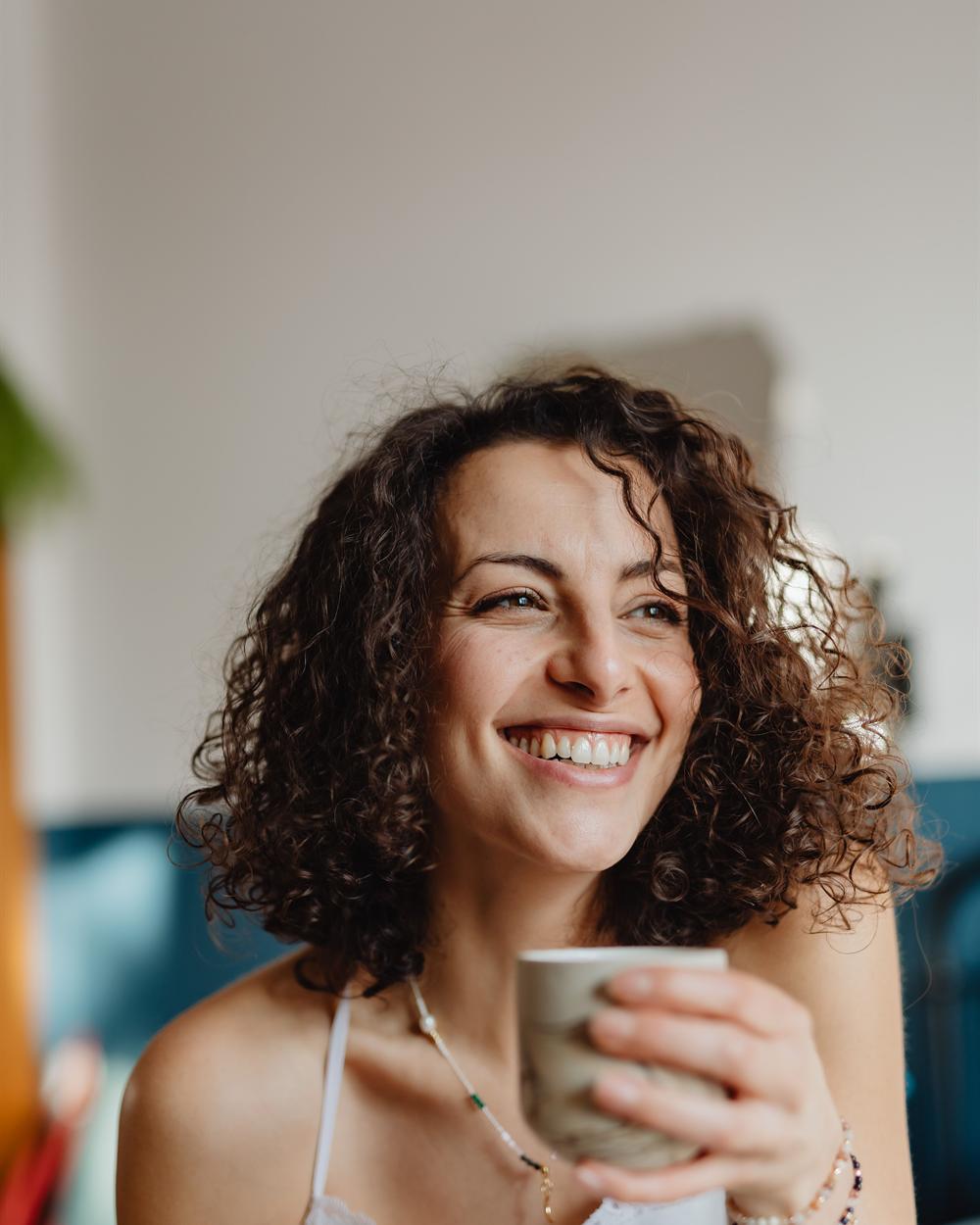 A woman at home, smiling, holding a mug